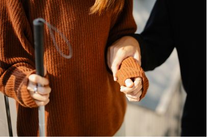 Close-up of a woman’s hand gently holding another’s arm who walks with a cane, symbolizing support, care, and commitment in faith.